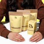 Person holding Endosoothe loose leaf tea packages and a Soothing Cream box on a white surface with a yellow background