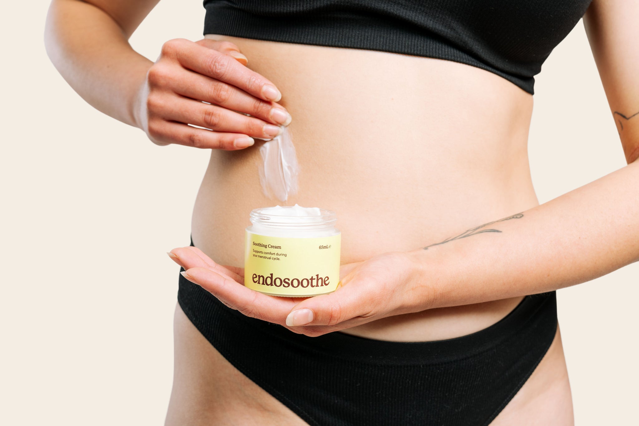 A woman applies a smooth, white cream to the side of her abdomen while holding a jar of Soothing Cream in the centre of the image.
