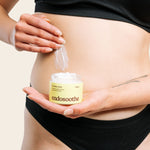 A woman applies a smooth, white cream to the side of her abdomen while holding a jar of Soothing Cream in the centre of the image.