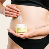 A woman applies a smooth, white cream to the side of her abdomen while holding a jar of Soothing Cream in the centre of the image.